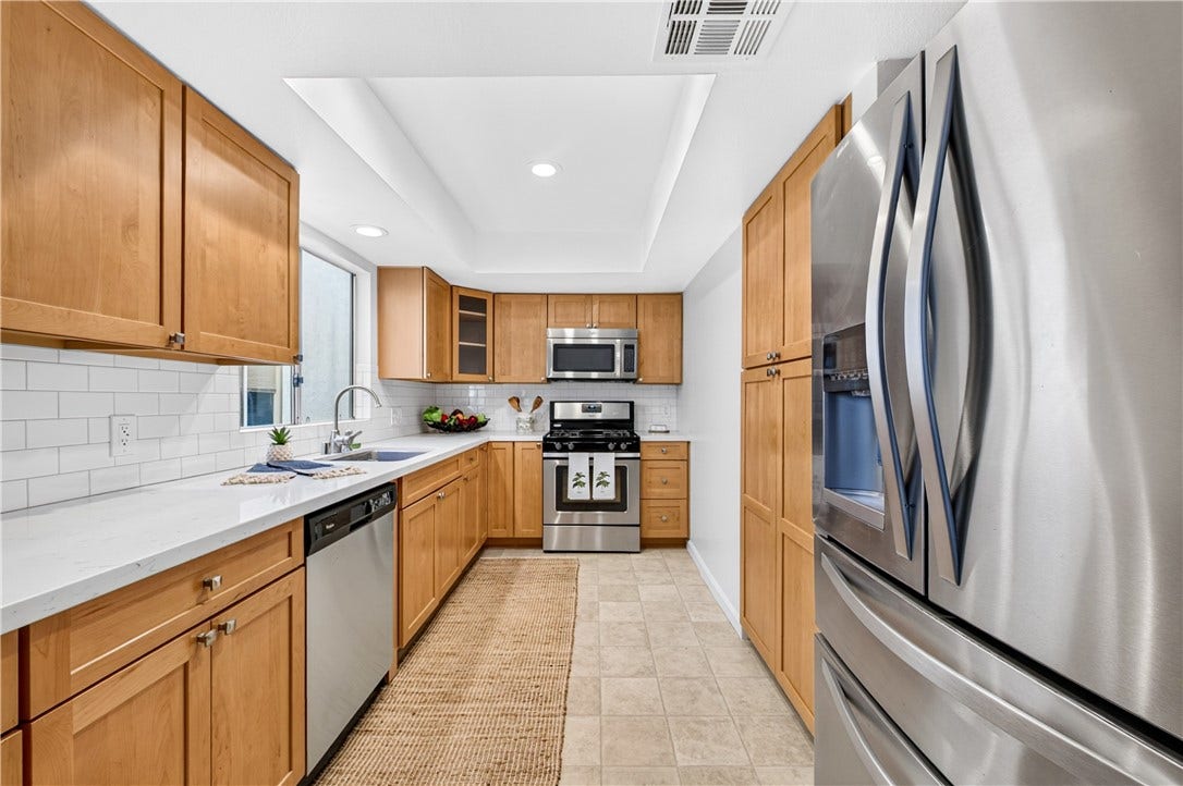 Beautifully appointed kitchen features warm wood cabinetry, quartz-style countertops, tile backsplash, and stainless-steel appliances.
